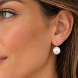 A close-up of a woman's ear wearing a single drop earring with a round white pearl and a small gold hook.