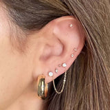 A close-up of a person's ear showcasing multiple gold and silver ear piercings, including a large gold hoop, a delicate gold chain, and several small stud earrings.