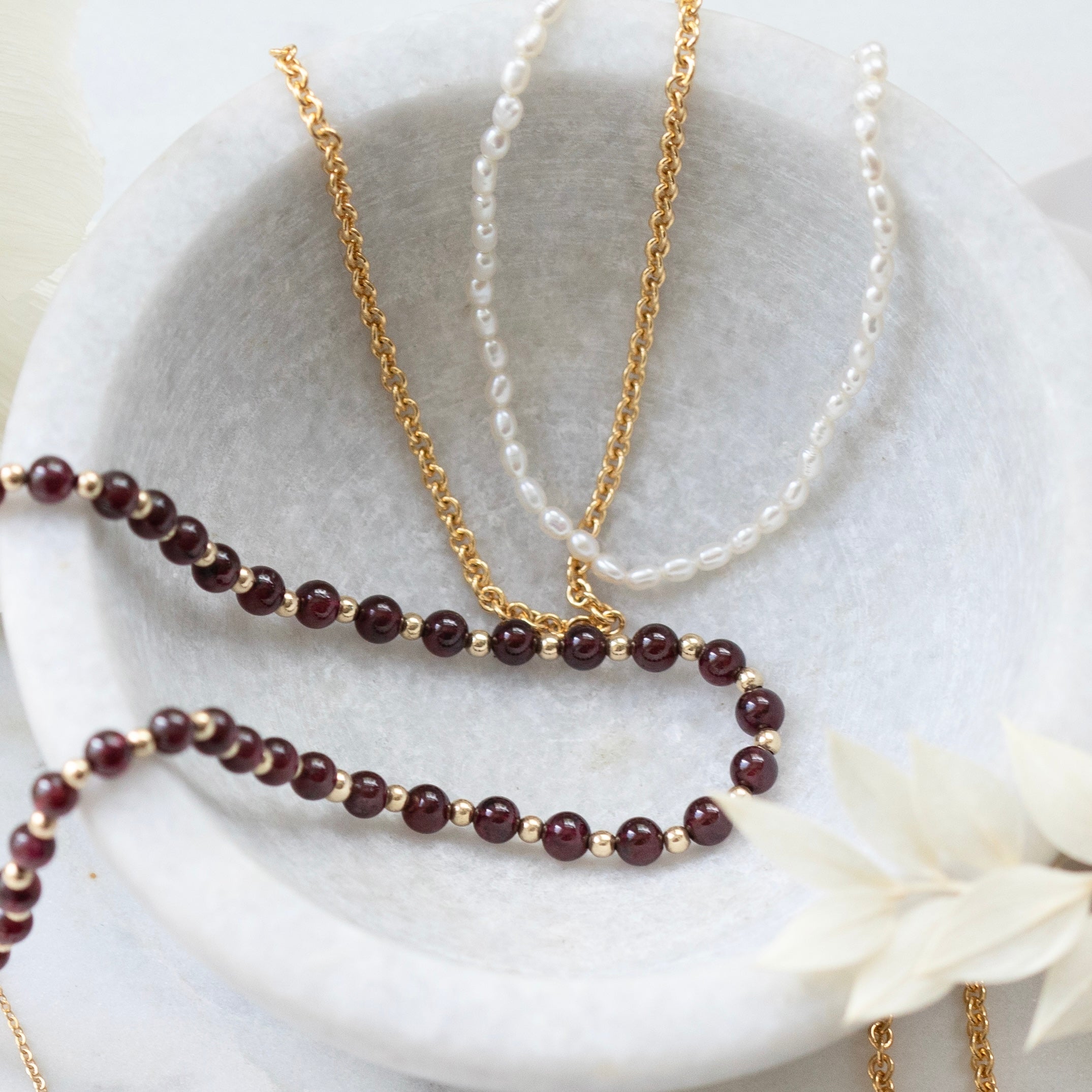 gold chain with white freshwater pearls, a gold chain with garnet beads separated by small gold beads, and a gold chain 