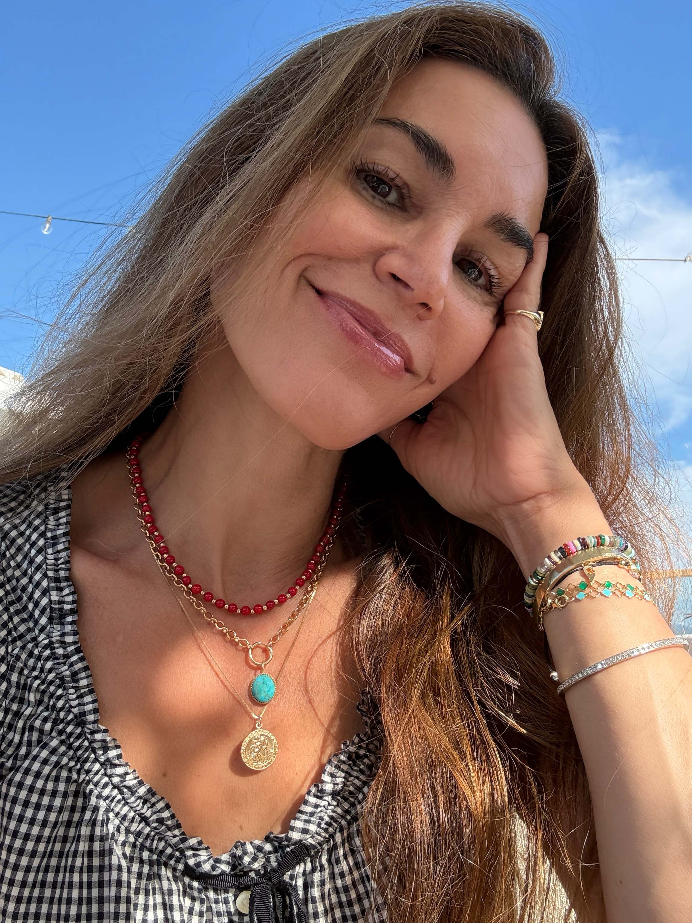  layered necklaces, including a red beaded necklace, a gold coin pendant necklace with a turquoise accent, and multiple bracelets