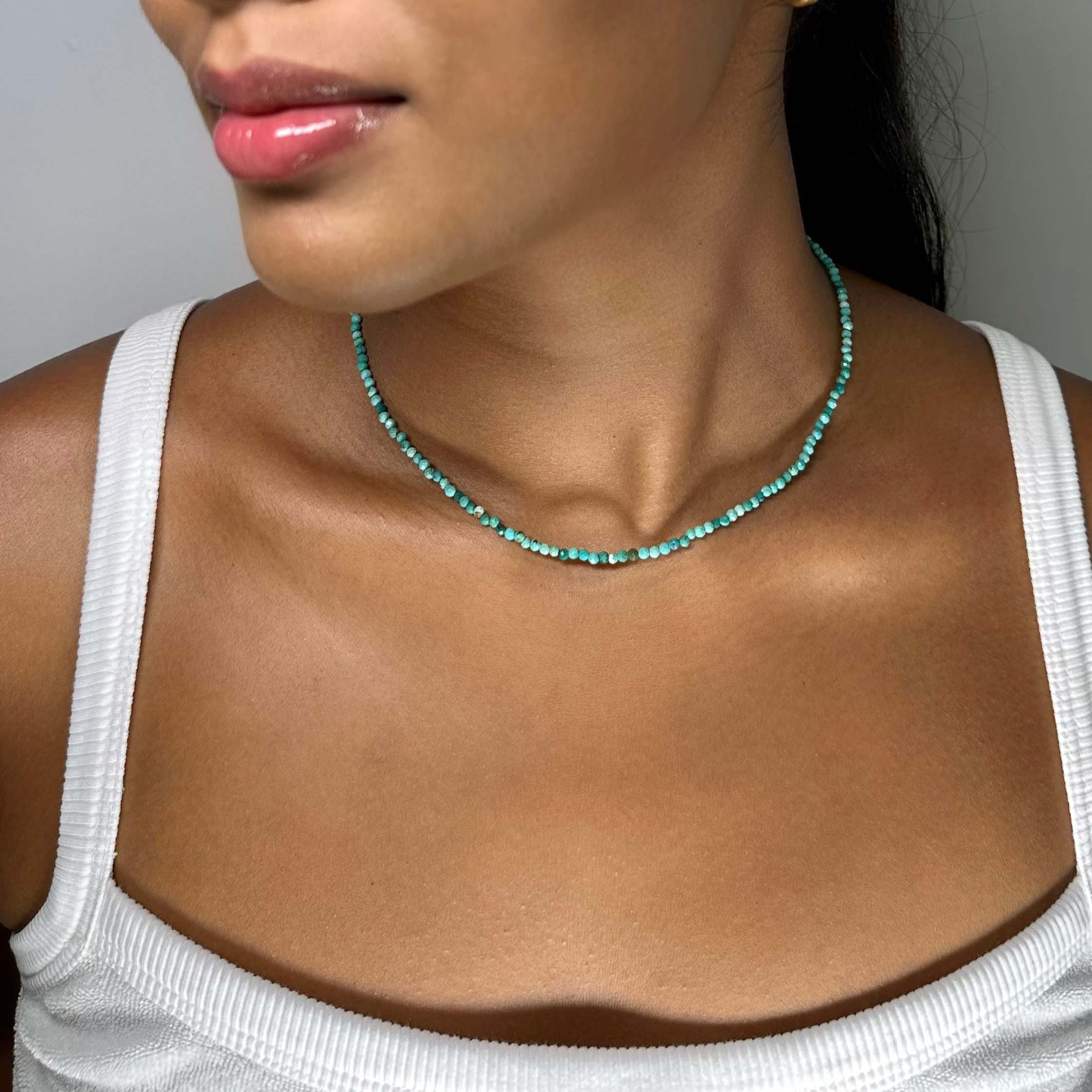 A close-up of a woman wearing a delicate turquoise beaded necklace 